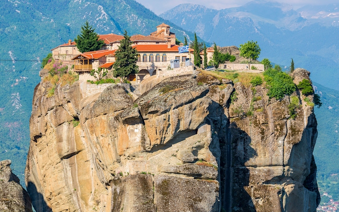 Meteora monastery perched on a rocky cliff with mountains in the background, Greece.