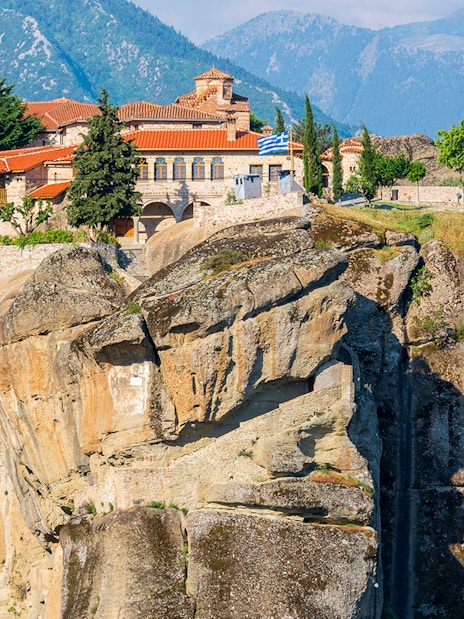 Meteora monastery perched on a rocky cliff with mountains in the background, Greece.