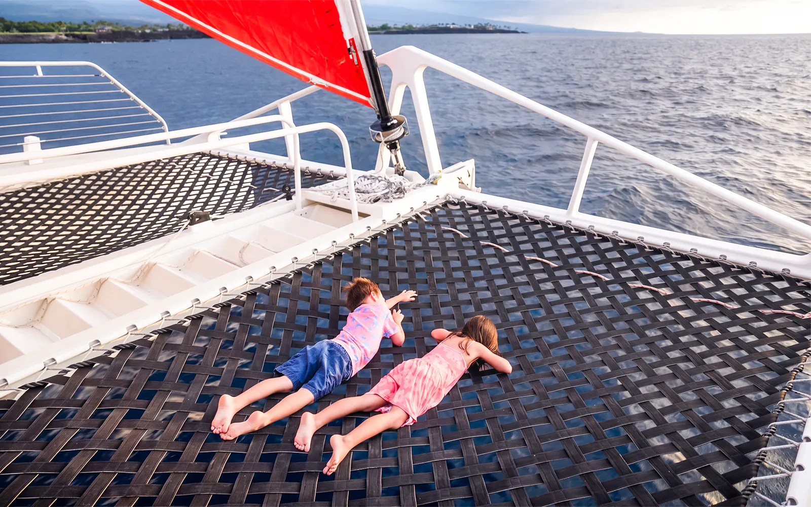 Kids lying on a catamaran viewing net over the ocean.