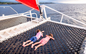 Kids lying on a catamaran viewing net over the ocean.