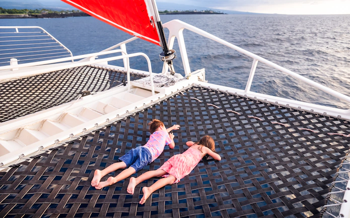 Kids lying on a catamaran viewing net over the ocean.