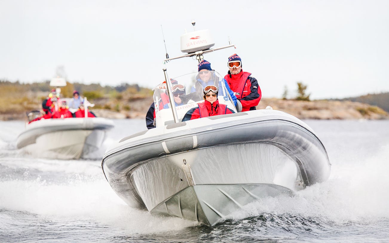 Passengers enjoying a thrilling ride on a Stockholm RIB speed boat with city skyline in the background.