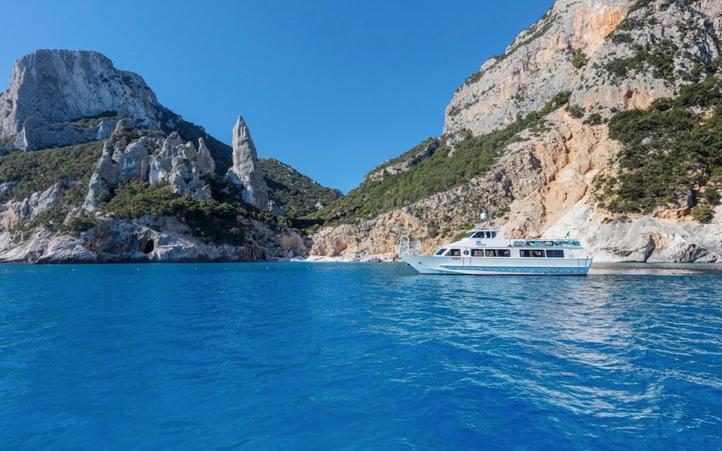 Boat cruising near rocky cliffs in the Gulf of Orosei, Italy.