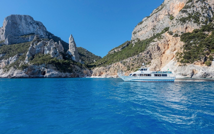 Boat cruising near rocky cliffs in the Gulf of Orosei, Italy.