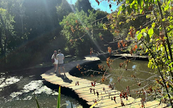 Visitors walking on a wooden footbridge at Parque Tricao, surrounded by lush greenery.