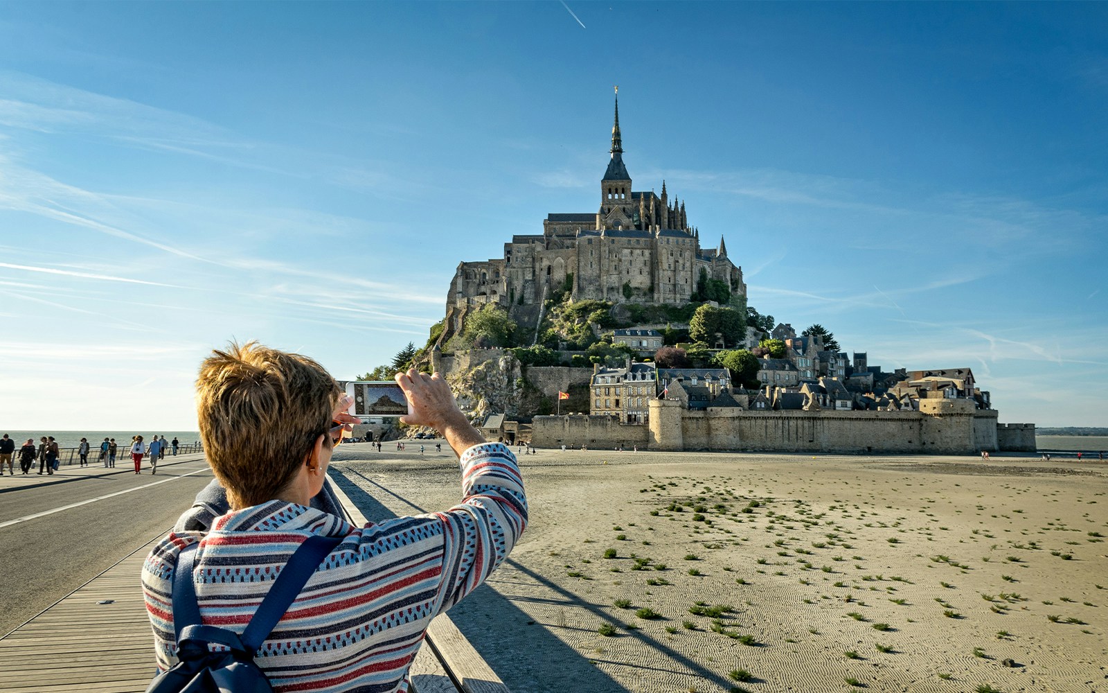 Tourist photographing Mont Saint Michel in Normandy, France, with iconic tidal island in background.