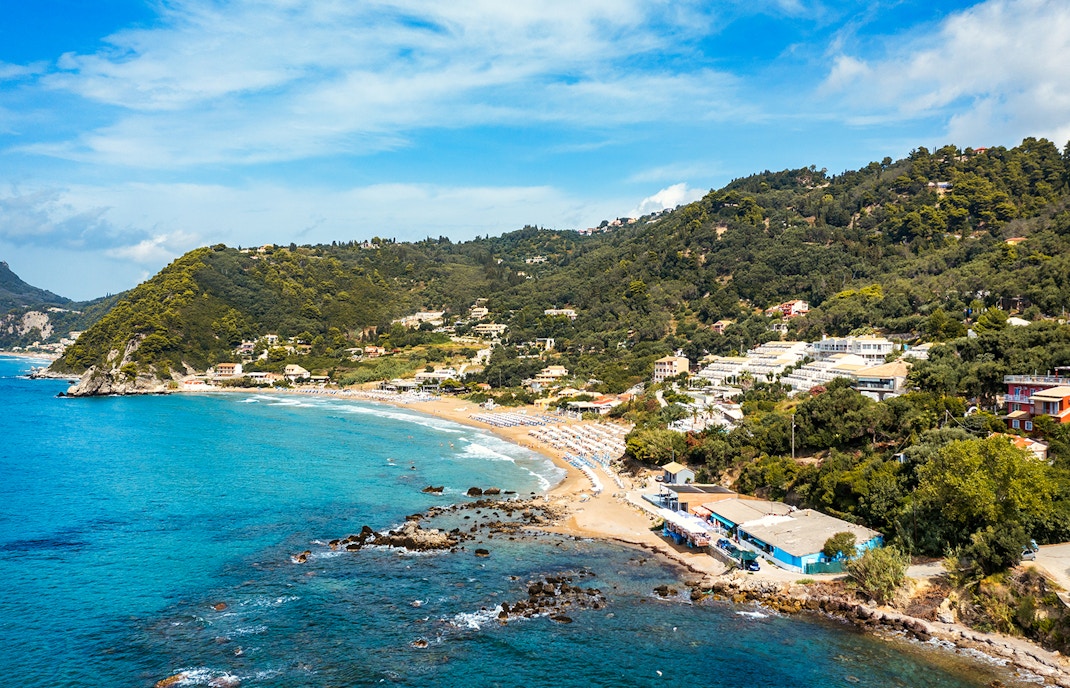 Glyfada Beach in Corfu, Greece with sunbathers and clear blue waters.