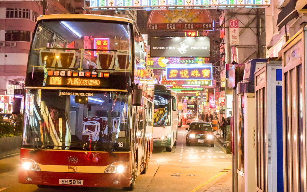 Hop-on-hop-off bus on a vibrant street in Hong Kong at night.
