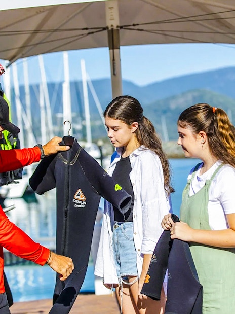 Tour guide handing wetsuits to participants on Thundercat Whitsundays Full Day Tour at marina.