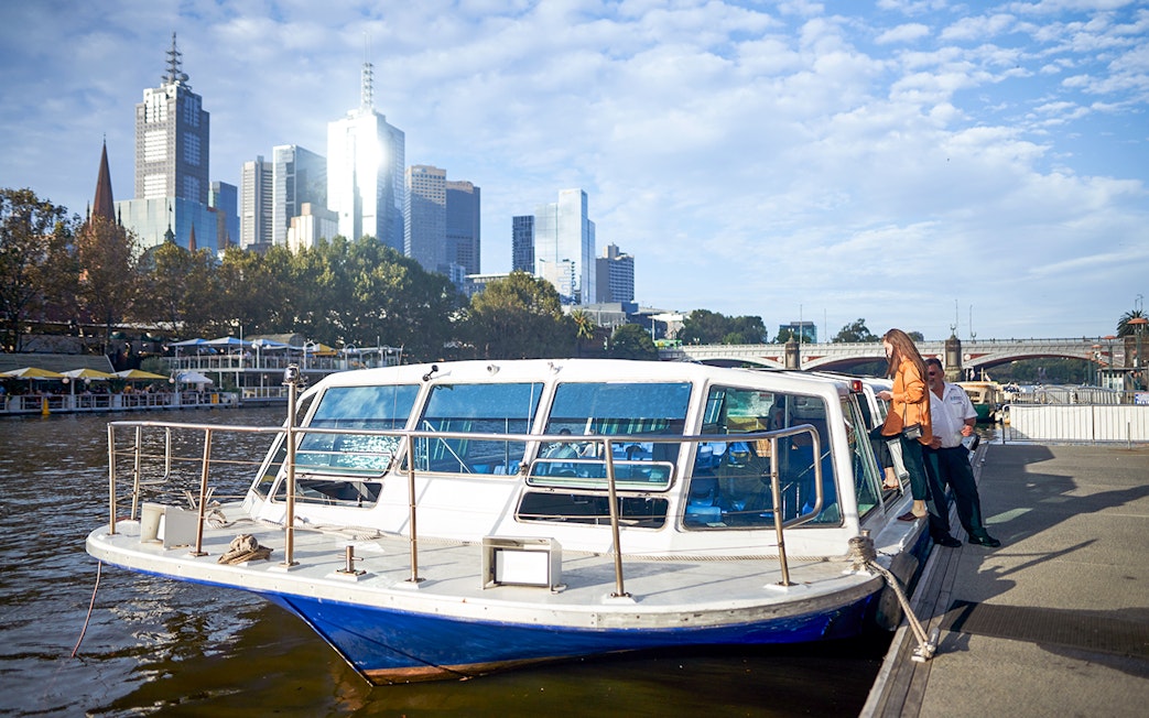 Melbourne River Cruise boat docked with city skyline in the background.