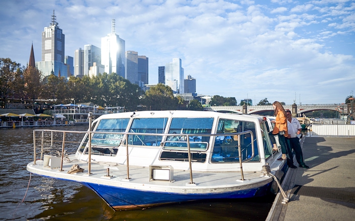 Melbourne River Cruise boat docked with city skyline in the background.