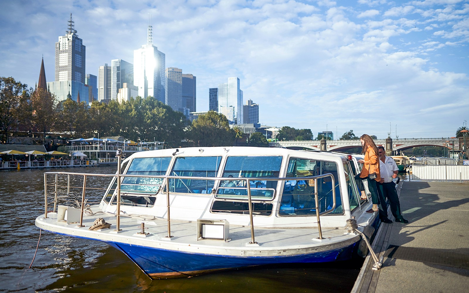 Melbourne River Cruise boat on Yarra River with city skyline in the background.