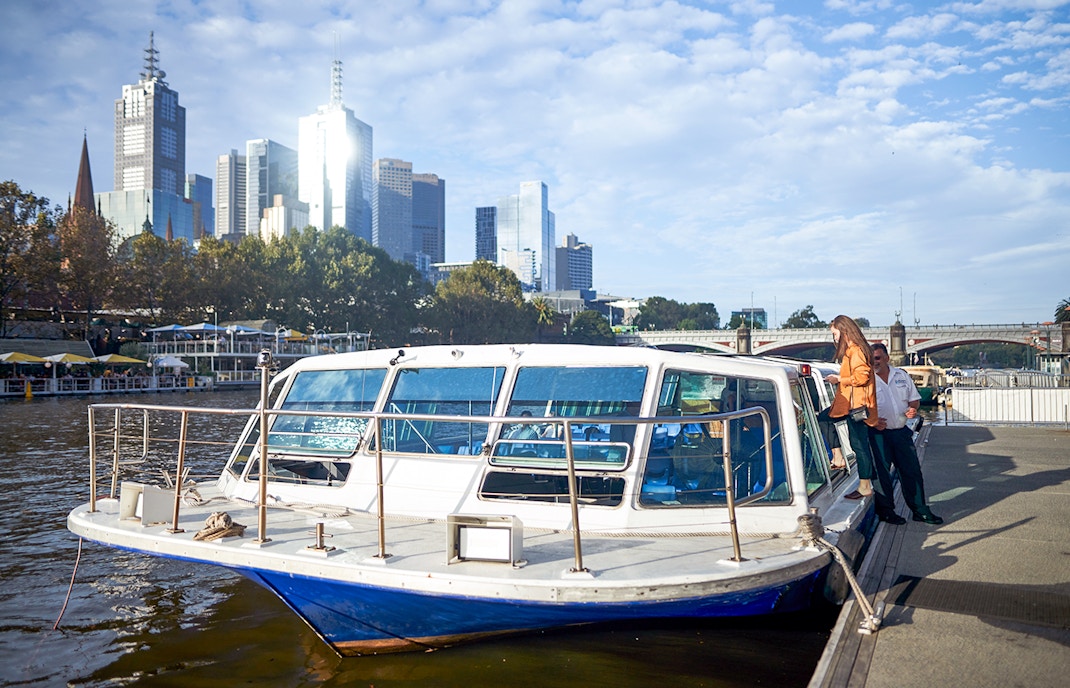 Melbourne River Cruise boat docked with city skyline in the background.
