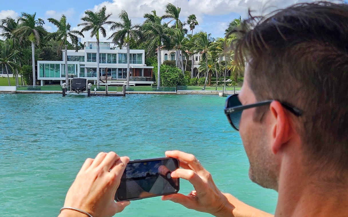 Man photographing luxury waterfront home from Miami yacht cruise.