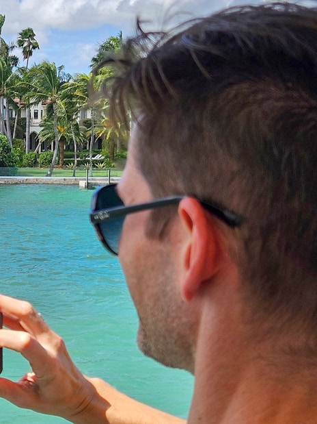 Man photographing luxury waterfront home from Miami yacht cruise.