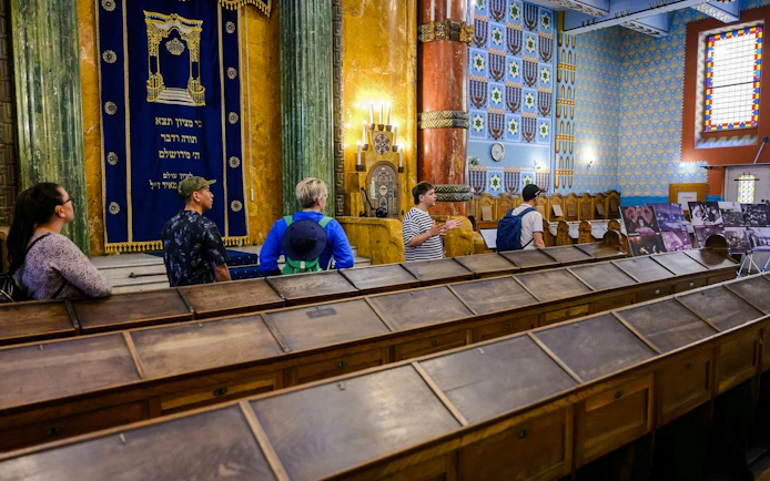 Visitors inside Kazinczy Synagogue in Budapest, viewing ornate interior and historical displays.