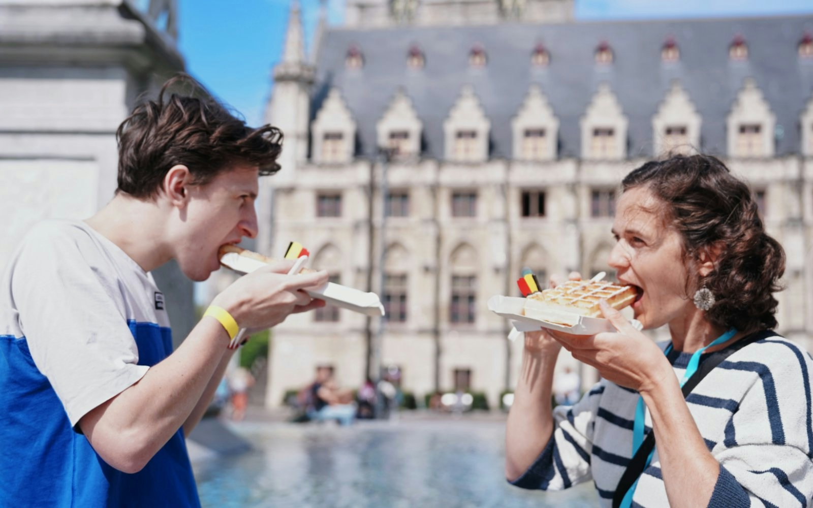People enjoying Belgian waffles in front of a historic building in Ghent.