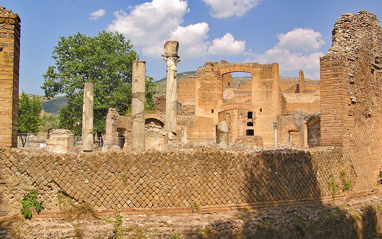 Ancient ruins and columns at Tivoli Villae, Italy, with a backdrop of trees and hills.