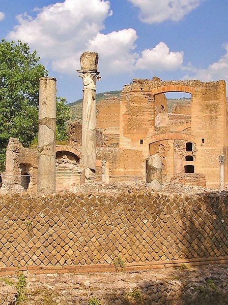 Ancient ruins and columns at Tivoli Villae, Italy, with a backdrop of trees and hills.