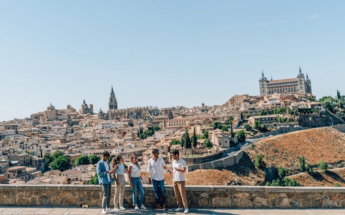 Tourists with guide overlooking Toledo's historic skyline, featuring Alcázar and cathedral.