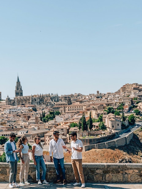 Tourists with guide overlooking Toledo's historic skyline, featuring Alcázar and cathedral.