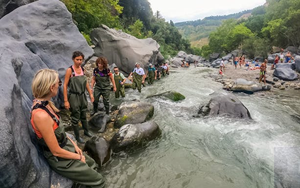 Group hiking through Alcantara River in Valle Alcantara, Sicily, wearing waders.
