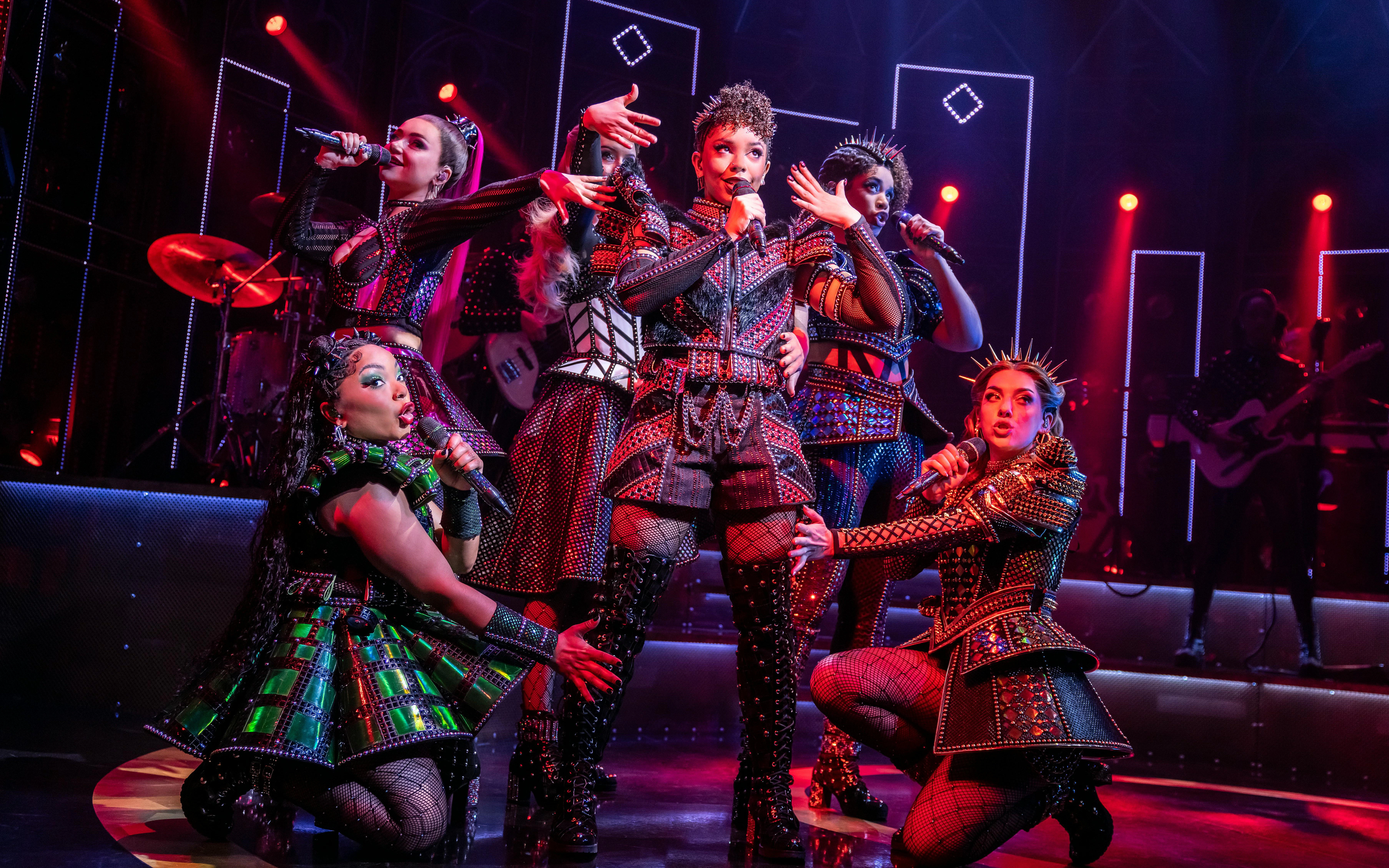 Six musical cast performing on stage in West End with vibrant costumes and dynamic lighting.