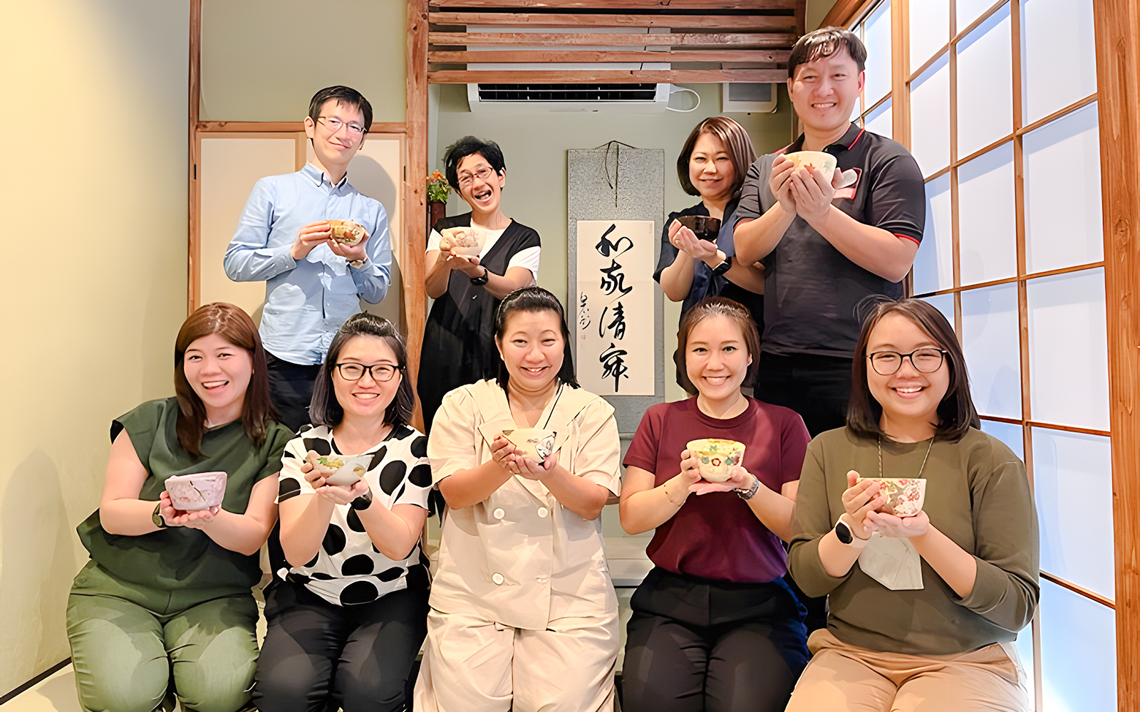Group enjoying tea ceremony in Osaka, holding traditional tea bowls.