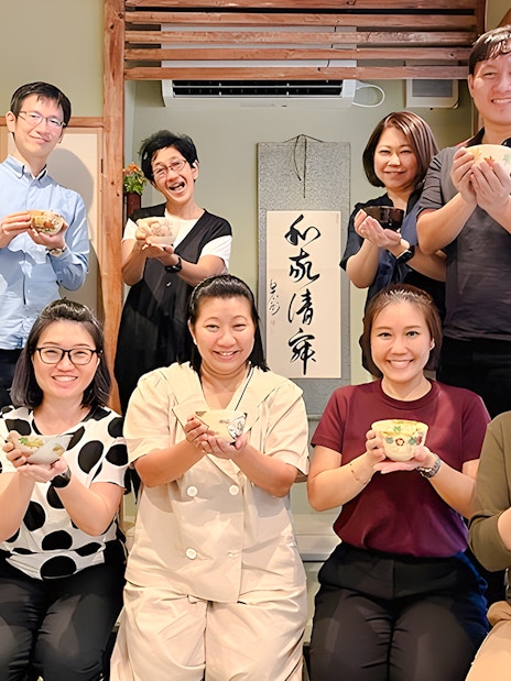 Group enjoying tea ceremony in Osaka, holding traditional tea bowls.