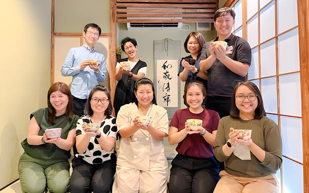Group enjoying tea ceremony in Osaka, holding traditional tea bowls.