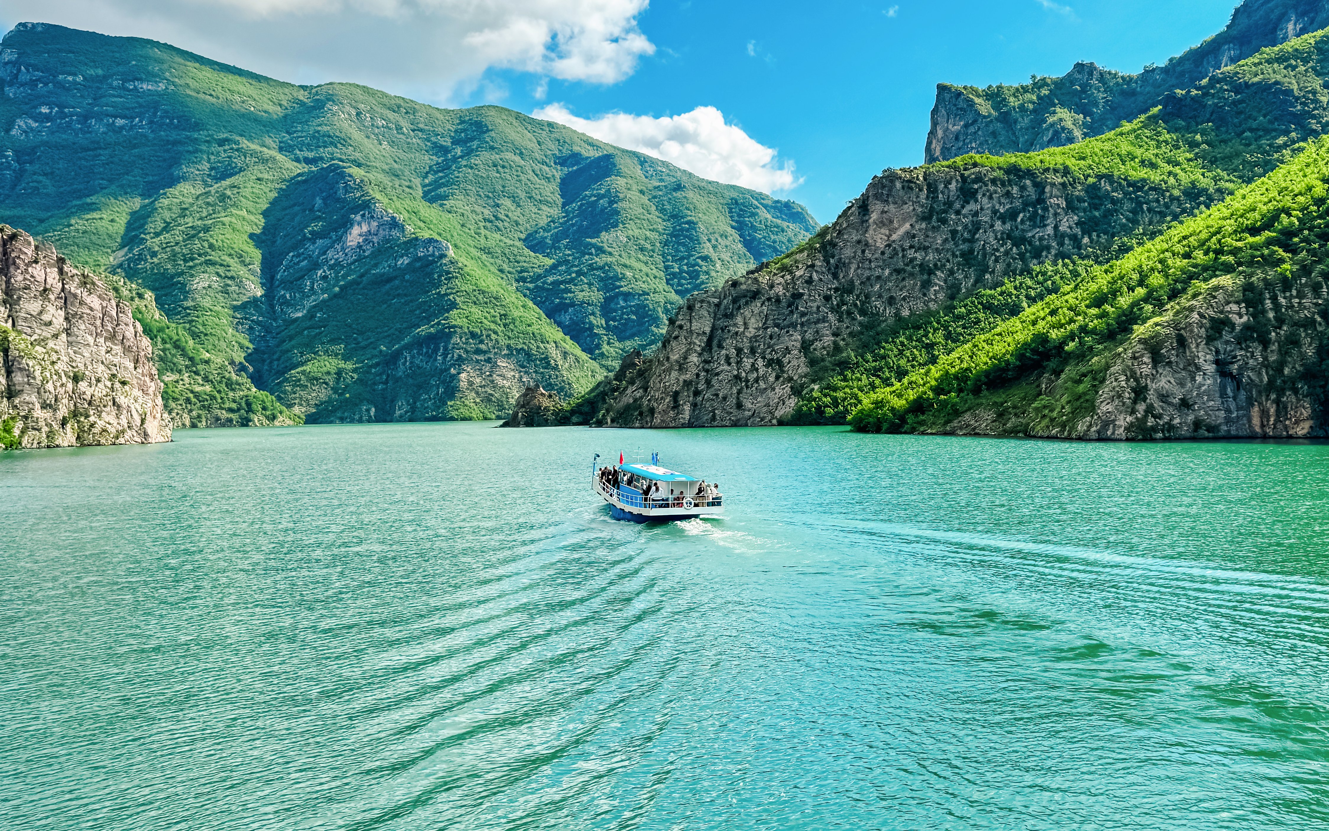 Ferry boat on Lake Koman, Albania, surrounded by lush green mountains.