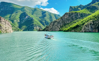 Ferry boat on Lake Koman, Albania, surrounded by lush green mountains.