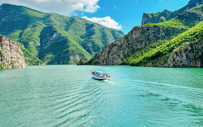 Ferry boat on Lake Koman, Albania, surrounded by lush green mountains.