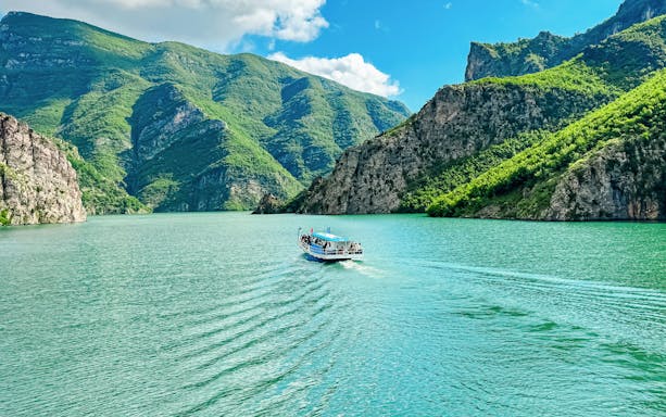 Ferry boat on Lake Koman, Albania, surrounded by lush green mountains.