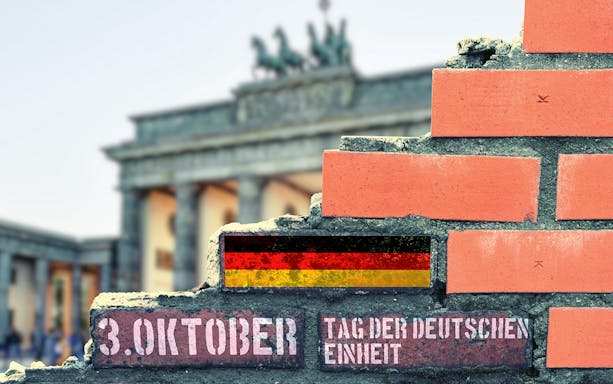 Brandenburg Gate with German Unity Day text and flag on a brick wall.