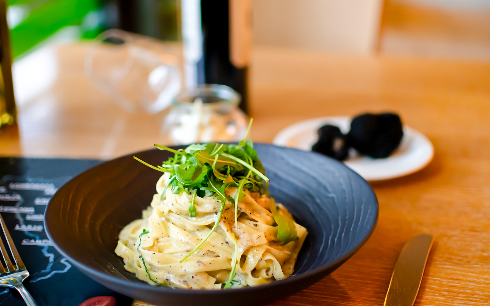 White truffle carbonara pasta garnished with arugula on a black plate.
