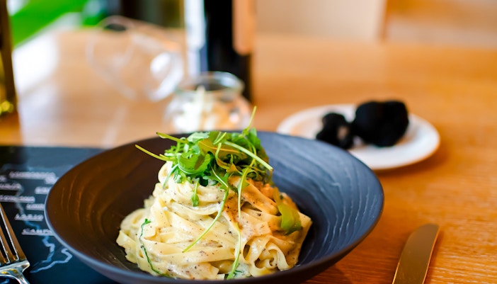 White truffle carbonara pasta garnished with arugula on a black plate.