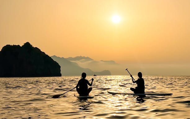 Paddleboarders on the water at sunset near Capri's coastline.