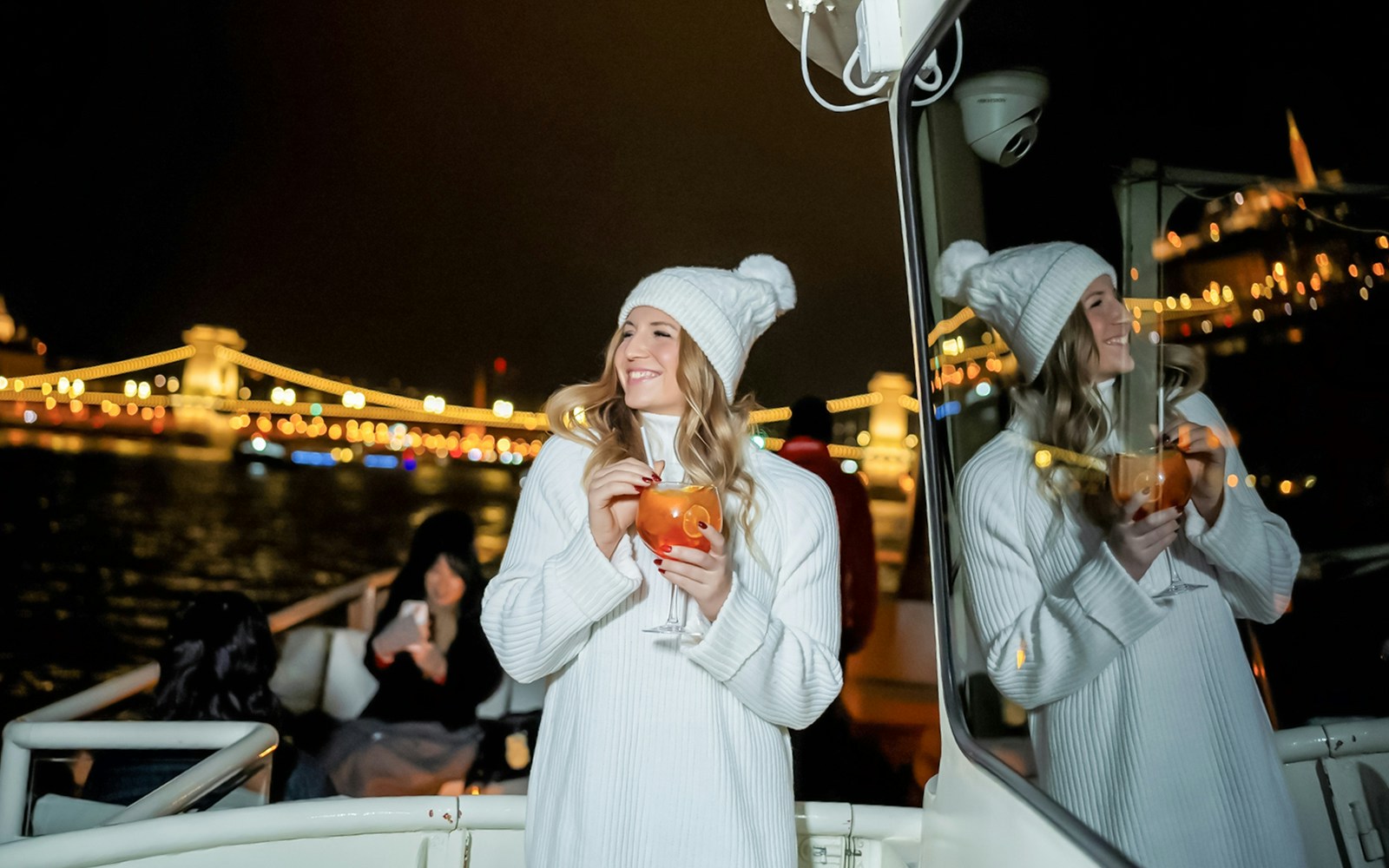 Guests enjoying drinks on a Budapest Danube River nighttime sightseeing cruise with city lights in the background.