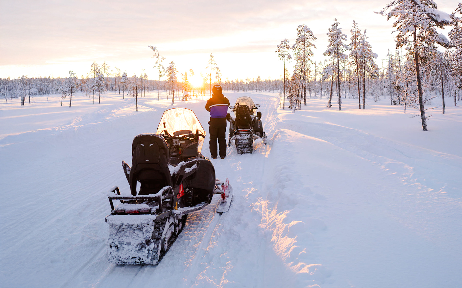 Snowmobiles on snowy trail at sunset in Lapland forest.