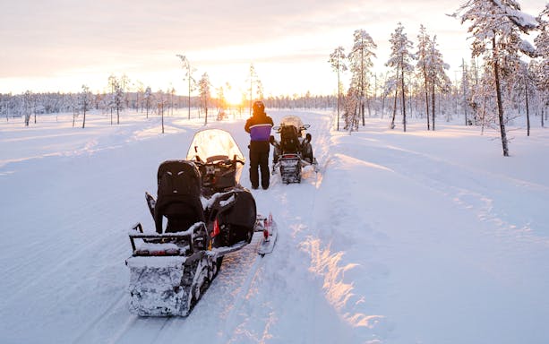 Snowmobiles on snowy trail at sunset in Lapland forest.