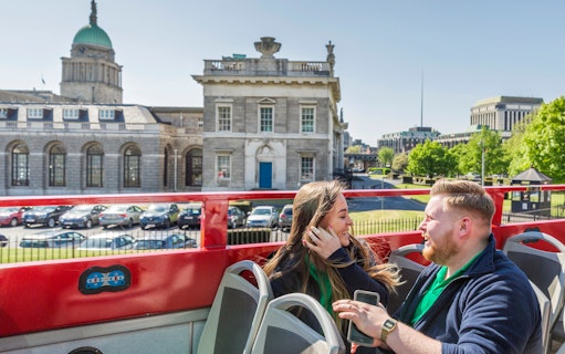 Open-top tour bus in Dublin passing historic buildings with passengers enjoying the view.