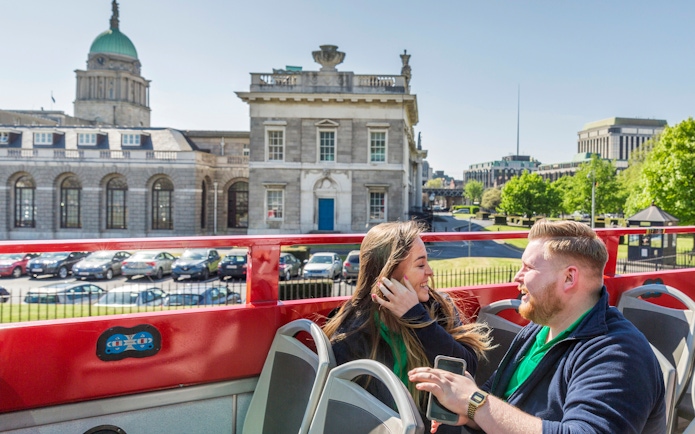 Open-top tour bus in Dublin passing historic buildings with passengers enjoying the view.