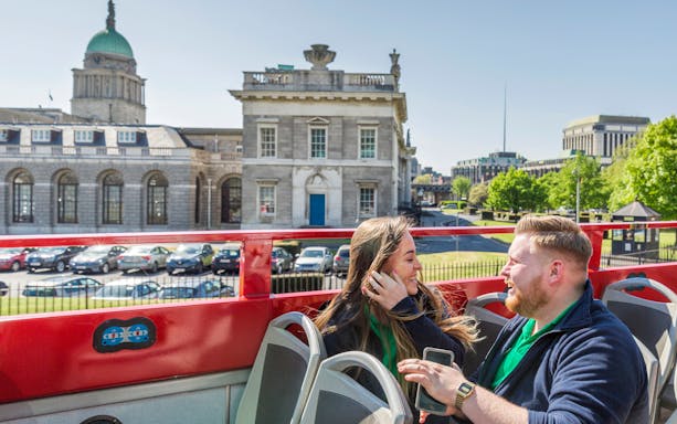 Open-top tour bus in Dublin passing historic buildings with passengers enjoying the view.