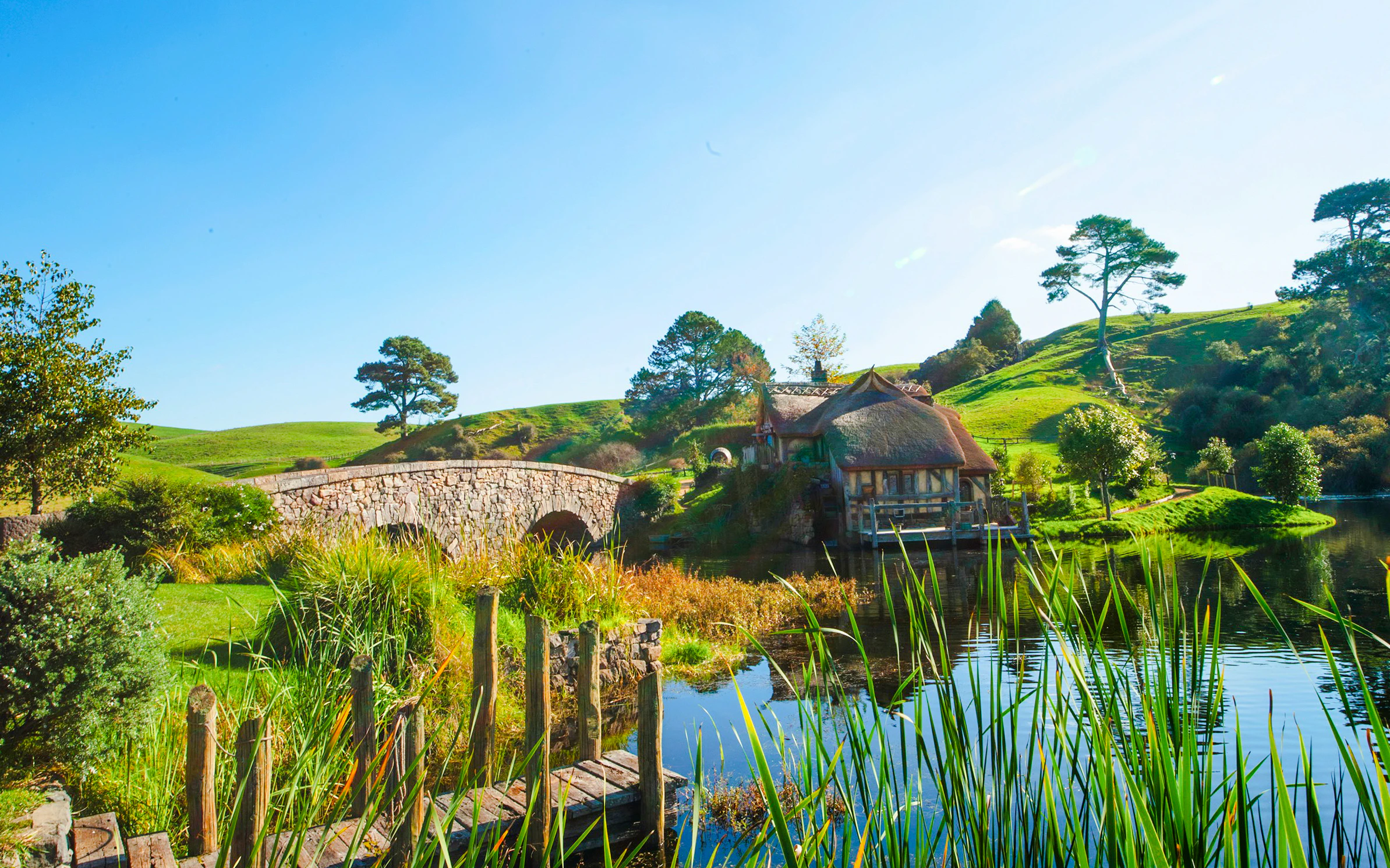 Double arched stone bridge at Hobbiton Movie Set, Matamata, New Zealand, with lush greenery and water.