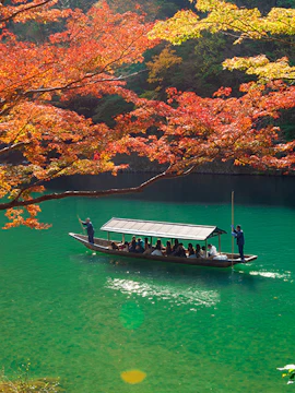 Tourist boat on Hozugawa River in Arashiyama Park, Kyoto, during autumn.
