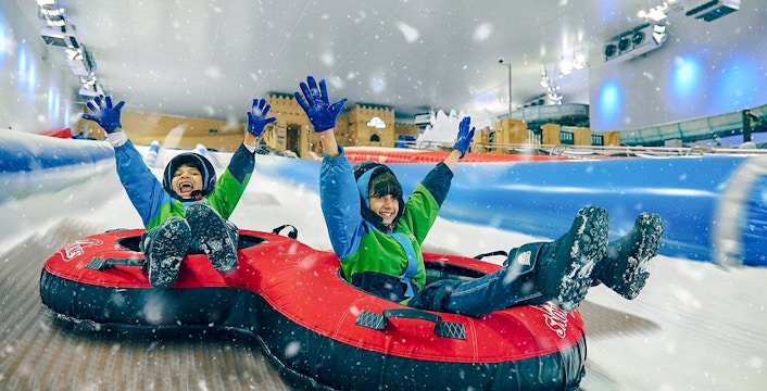 Children tubing down a snowy slide at Snow Dunes Theme Park.