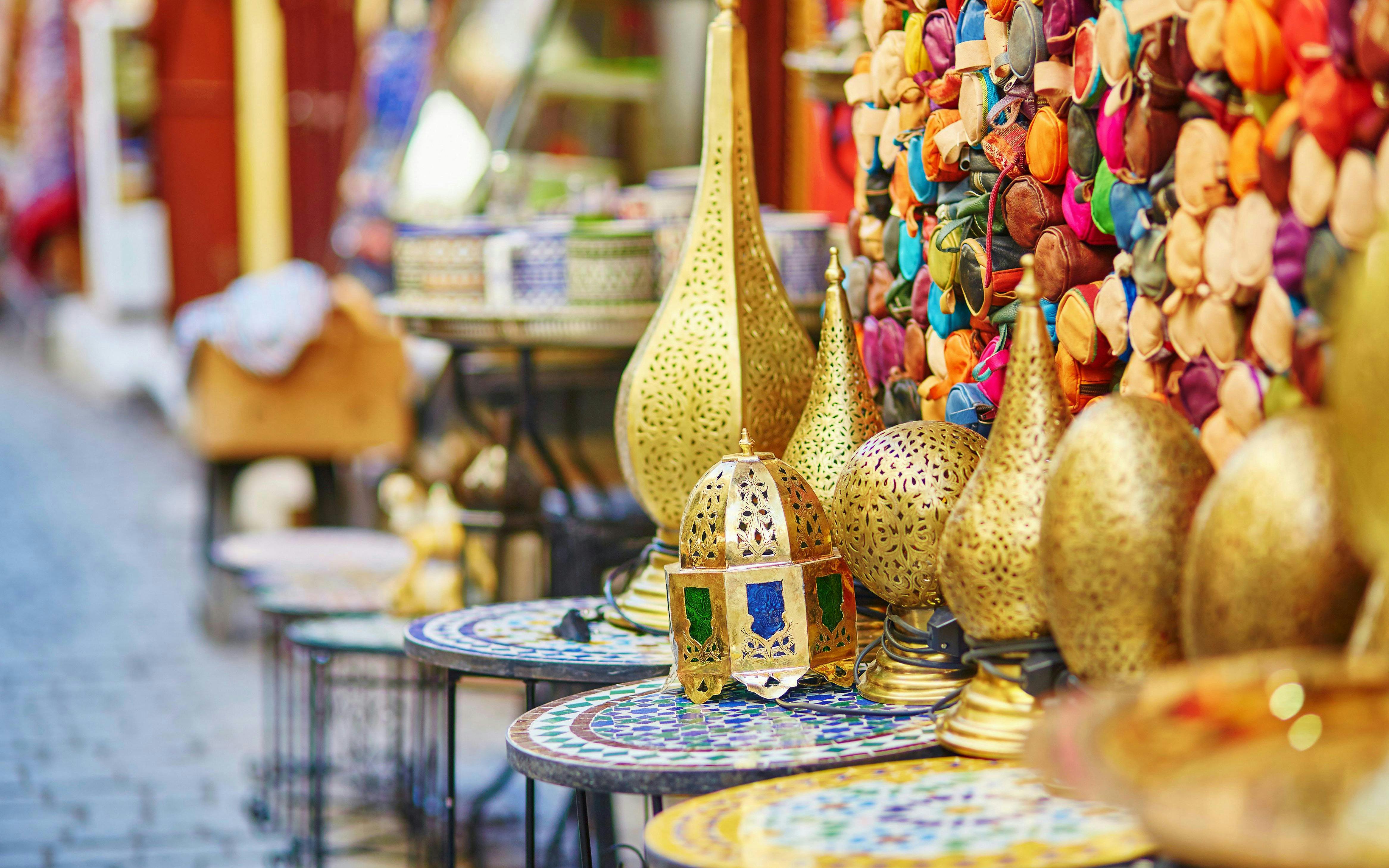 Traditional brass lamps displayed on mosaic tables in a vibrant market setting.