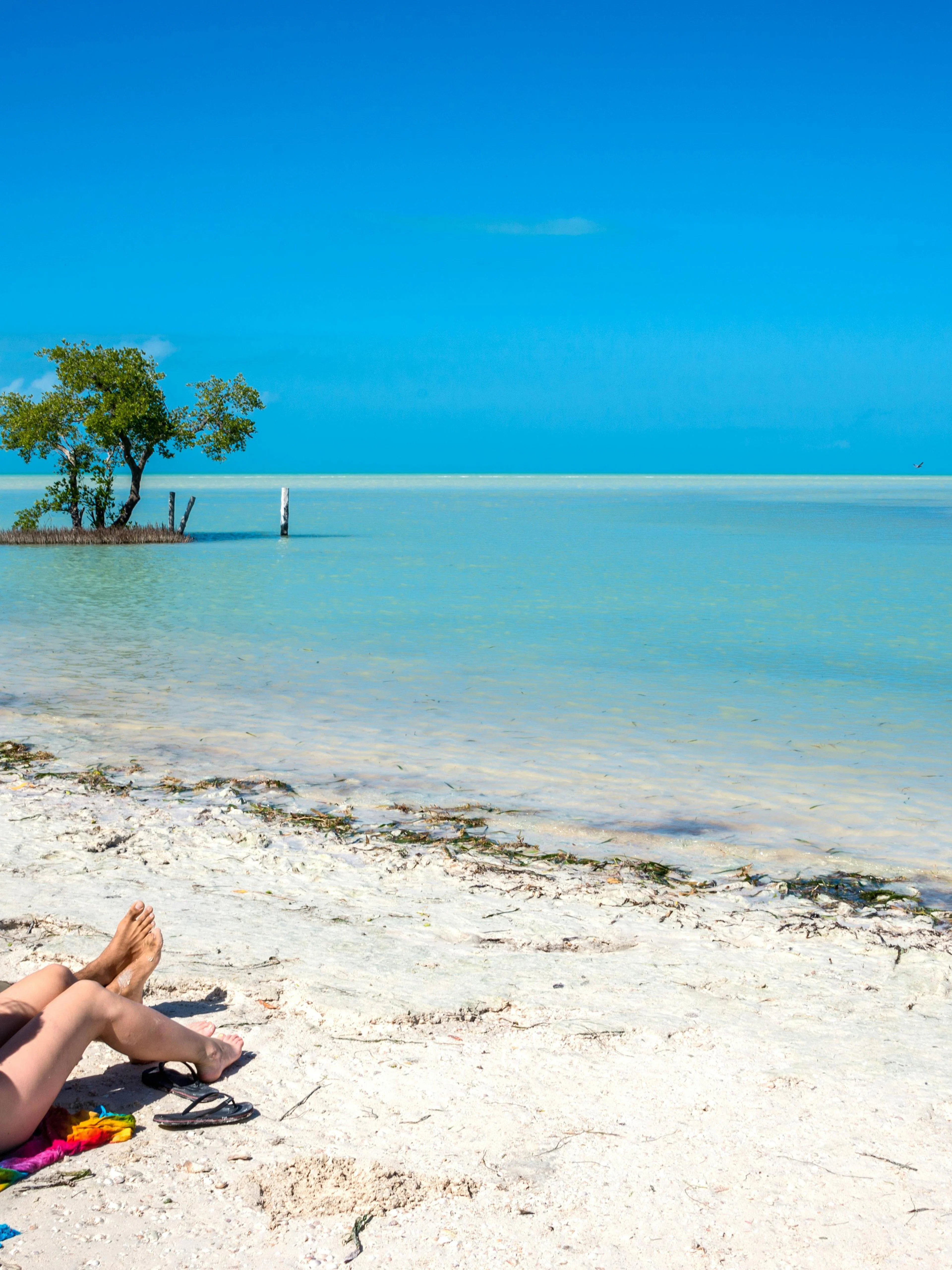Couple relaxing on a sandy beach at Holbox Island, Mexico, with turquoise water and clear sky.