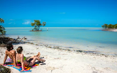 Couple relaxing on a sandy beach at Holbox Island, Mexico, with turquoise water and clear sky.